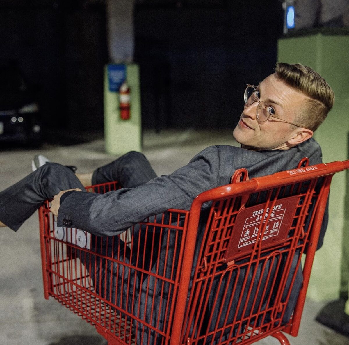 Danny Killea in a grey suit lounging in a Trader Joe's shopping cart